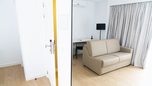 Una habitación con un sofá color beige, un escritorio y un televisor de pantalla plana.