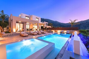 A modern house with a swimming pool, outdoor seating, and a mountain backdrop.