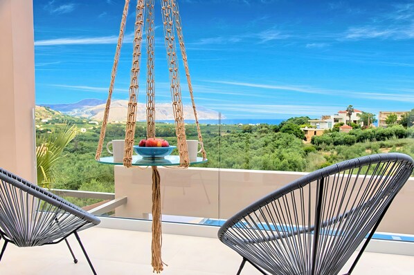 A balcony with wicker chairs, a hanging chair, and a table with fruit and a cup.