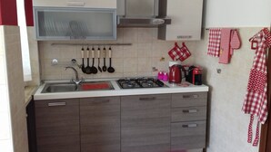 Eine kleine Küche mit Spüle, Herd und Schränken. Verschiedene Küchenutensilien hängen an der Wand, auf der Arbeitsfläche stehen ein Wasserkocher und eine Kaffeemaschine.