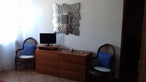 Ein Zimmer mit einem hölzernen Schminktisch, zwei Stühlen, einem auf dem Schminktisch stehenden Fernseher und einem an der Wand befestigten Spiegel.