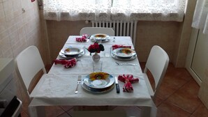 Ein Esstisch für vier Personen, mit weißen Stühlen, einer Blumenvase und Tellern mit Sonnenblumenmuster.