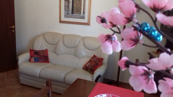 A beige sofa with two decorative pillows, a framed picture on the wall, and a pink flower arrangement in the foreground.