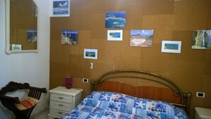 A bedroom with a bed, a dresser, a nightstand, a mirror, and corkboard with photos. - Portion of a Villa Near the sea (Capoterra)