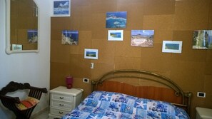 A bedroom with a bed, a dresser, a nightstand, a mirror, and corkboard with photos.
