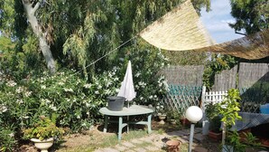 A garden with a table and chairs, a hanging shade, and a small tree. - Portion of a Villa Near the sea (Capoterra)