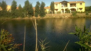 A building with a large water body in front, surrounded by trees. - Portion of a Villa Near the sea (Capoterra)