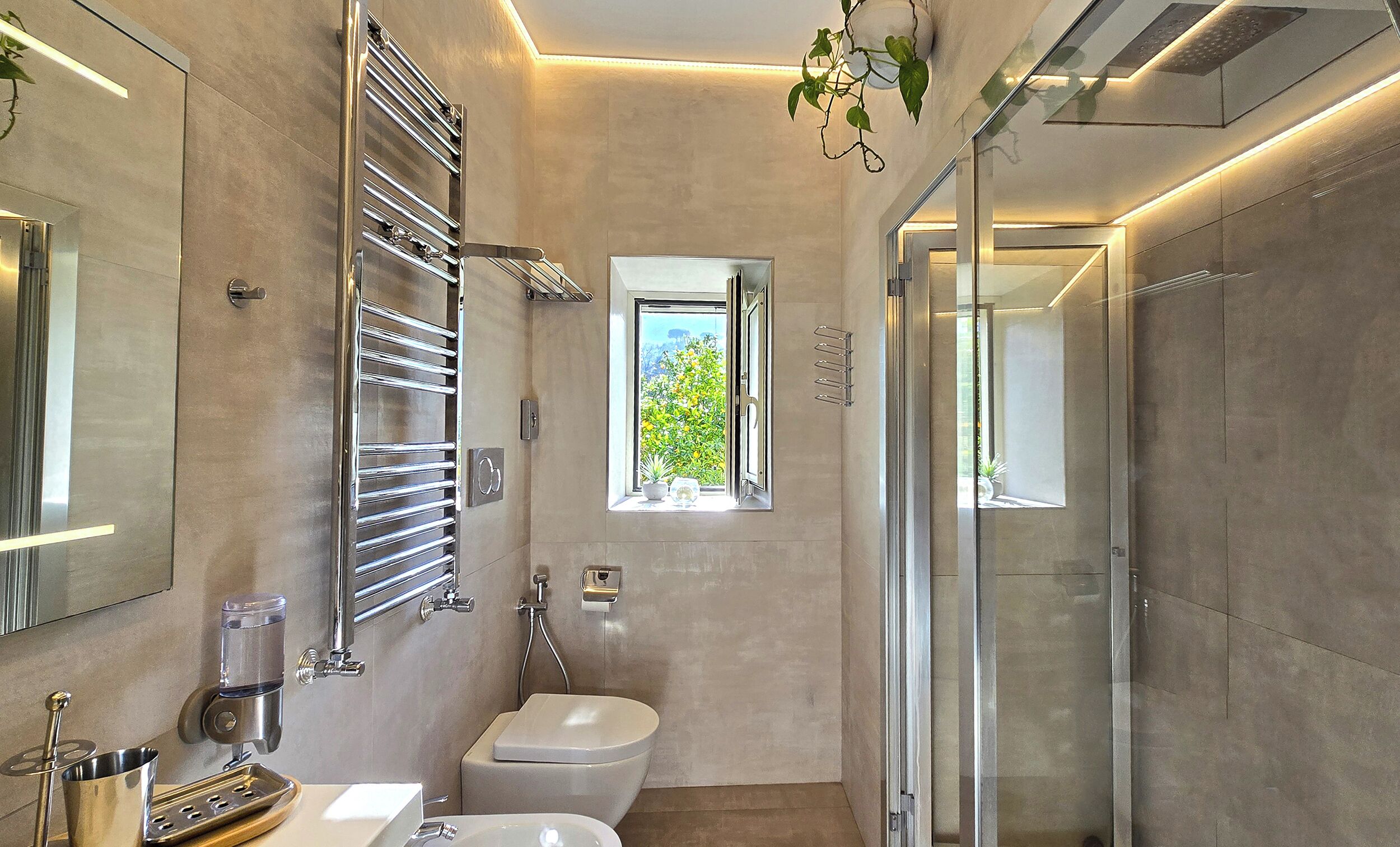 Un baño moderno con cabina de ducha de vidrio, inodoro y lavamanos. Hay una ventana con vistas a zonas verdes.