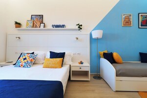 A hotel room with a bed, bedside tables, a nightstand, a lamp, and a shelf with decorative items.