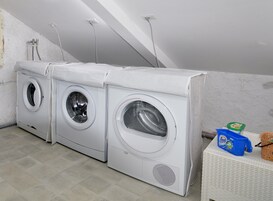 A laundry room with three stacked front-loading washing machines, a white tiled floor, and a ceiling with visible plumbing.
