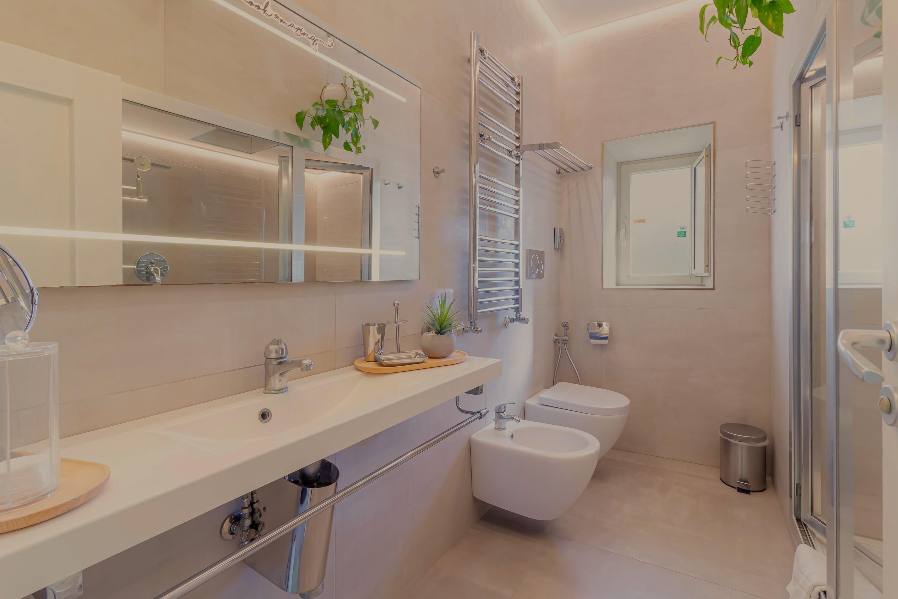 A modern bathroom with a large mirror, a sink, a bidet, and a glass shower enclosure.