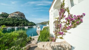 A coastal view with a white building, a stone staircase, and a mountain in the background. - Beautiful apartment in Baja Sardinia (Baja Sardinia)