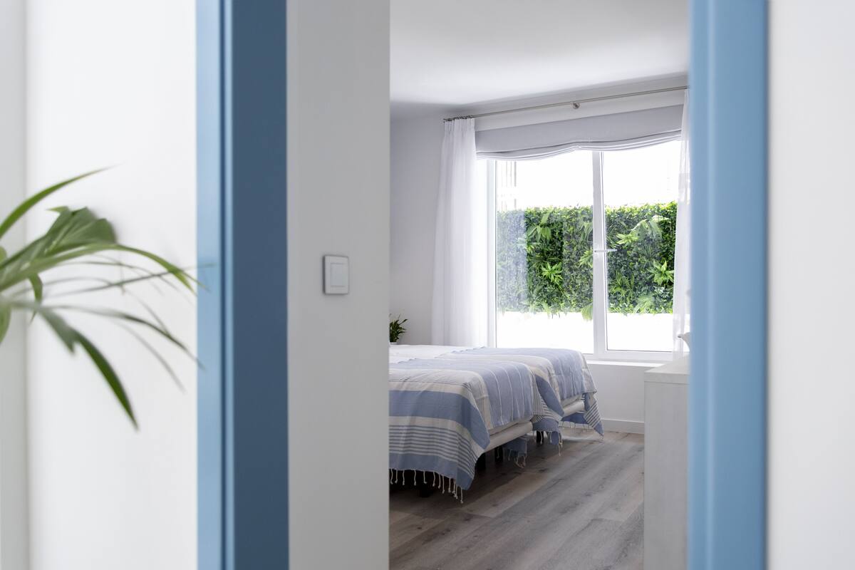 Un dormitorio con dos camas, un ventanal y vistas al verdor exterior.