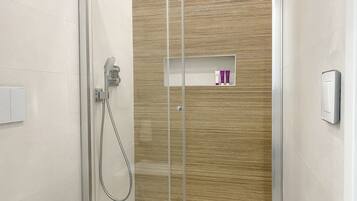 Un baño moderno con cabina de ducha de vidrio, estante empotrado con artículos de aseo y un interruptor de luz en la pared.