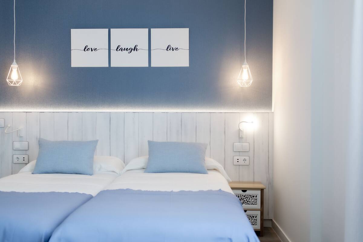 Un dormitorio con una cama, dos mesitas de noche y una lámpara fijada a la pared.