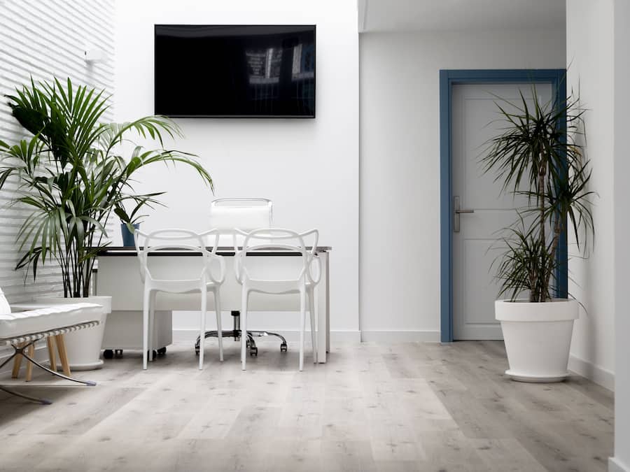Une pièce moderne et minimaliste, avec un bureau blanc, deux chaises blanches, un téléviseur à écran plat fixé au mur et des plantes en pot.