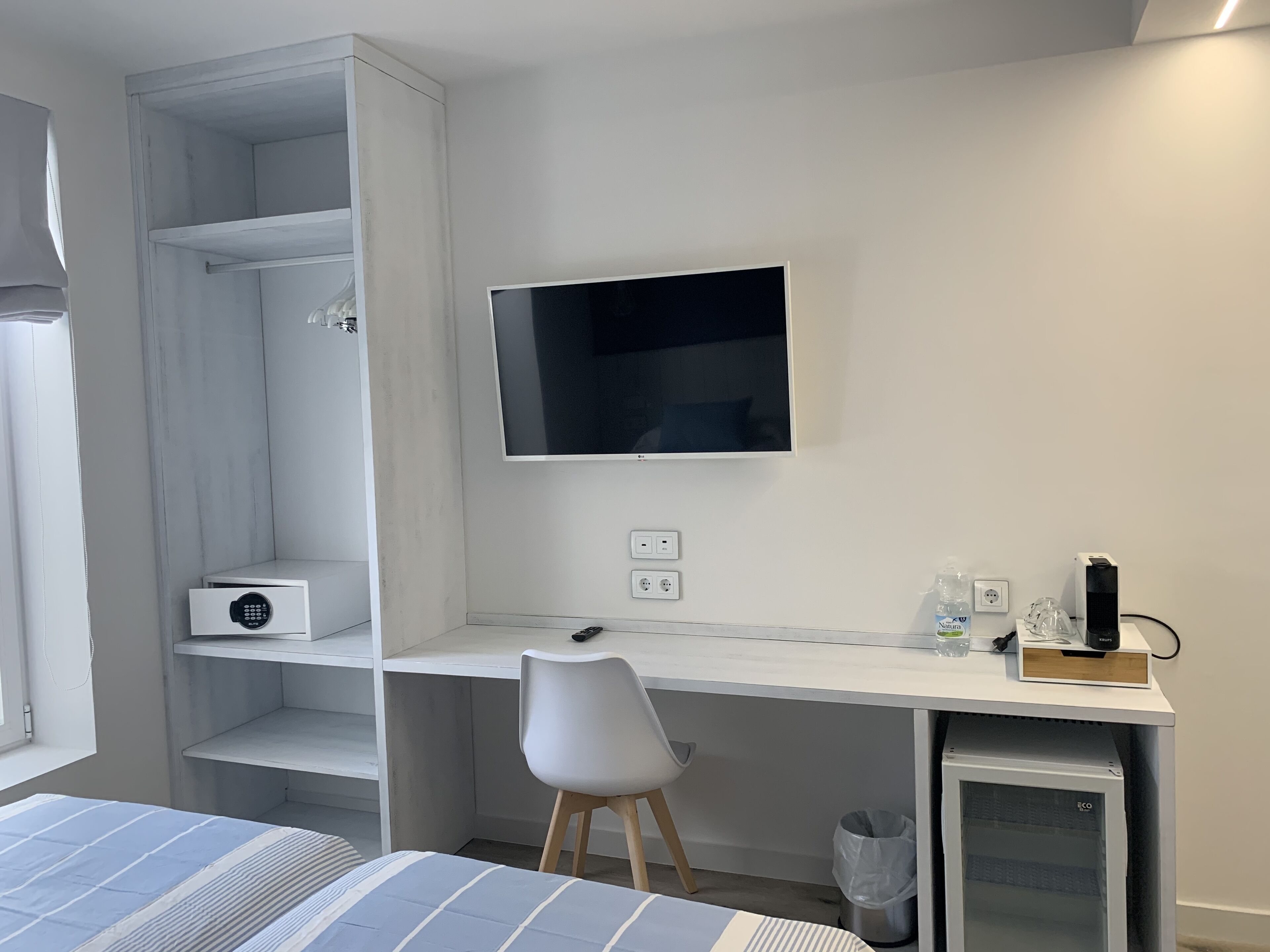 A modern bedroom with a bed, a desk, a chair, a TV, and a mini-fridge.