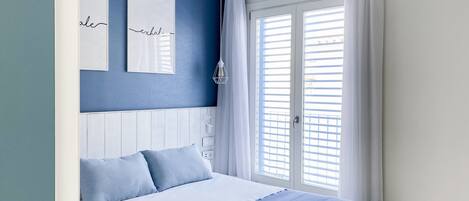 A bedroom with a bed, a window with curtains, a wall with a framed sign, and a light fixture.
