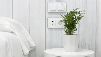 Una mesita de noche blanca con un cajón, una planta en maceta y un enchufe con un tapón.