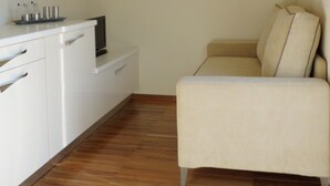 Een compacte, moderne kamer met een witte bank, een houten kast en een klein tafeltje met een afstandsbediening.