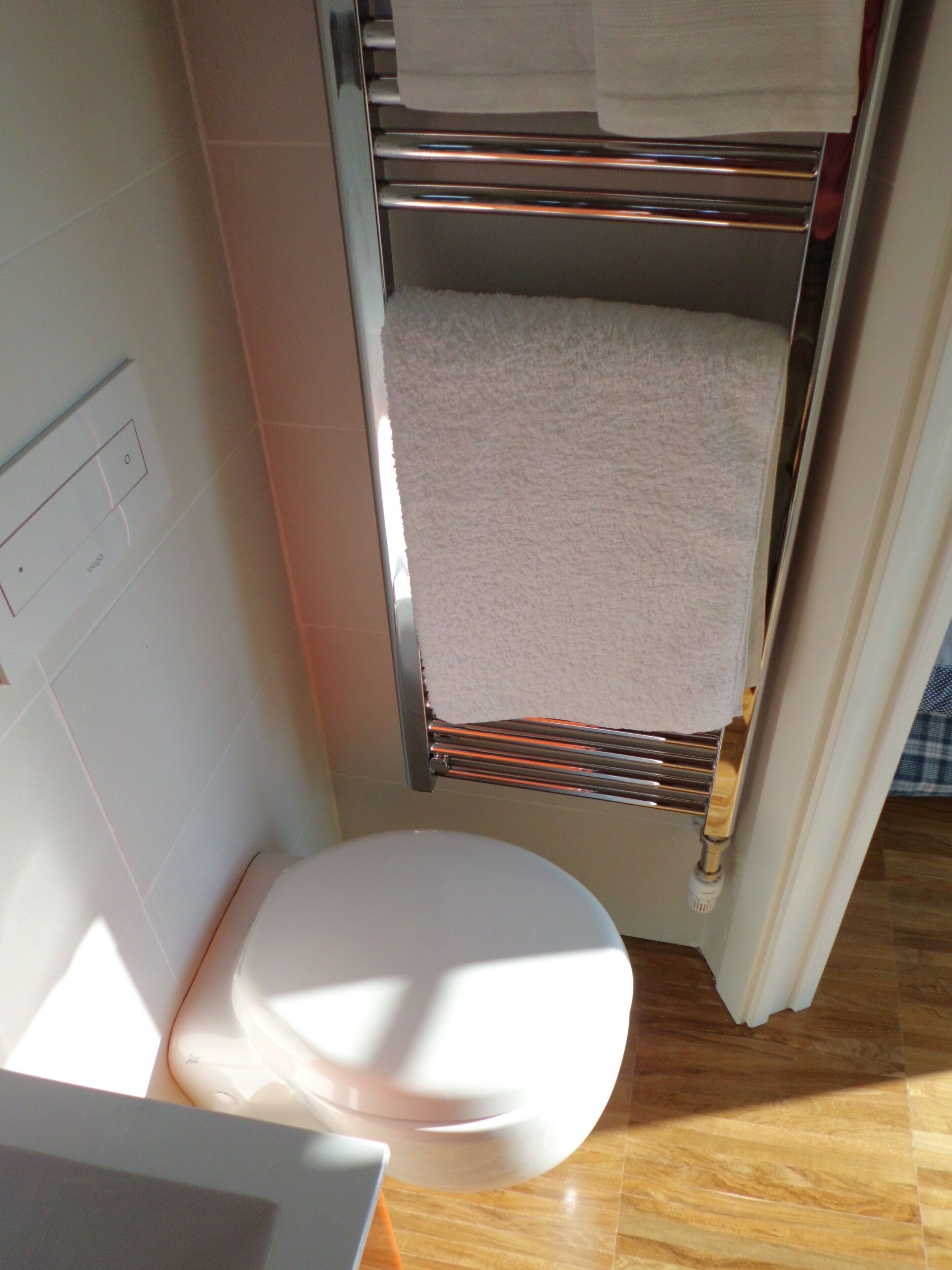 A compact bathroom with a white toilet, a towel rack with two towels, and a visible light switch on the wall.