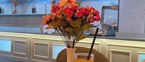 A dining table with a variety of dishes, a vase with flowers, and a glass of orange juice.