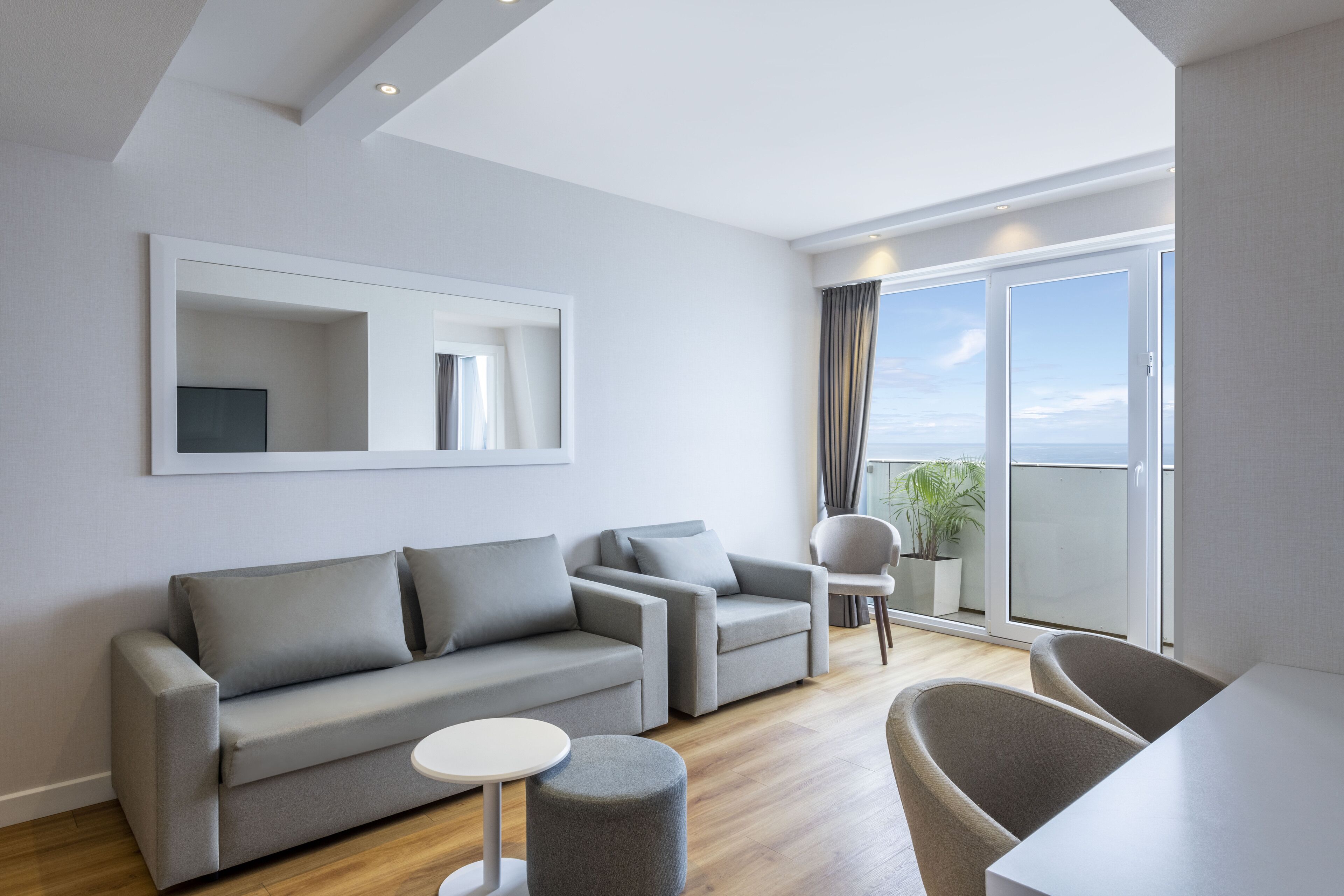 A modern living room with a grey sofa, a round coffee table, and a dining area with a white table and chairs.