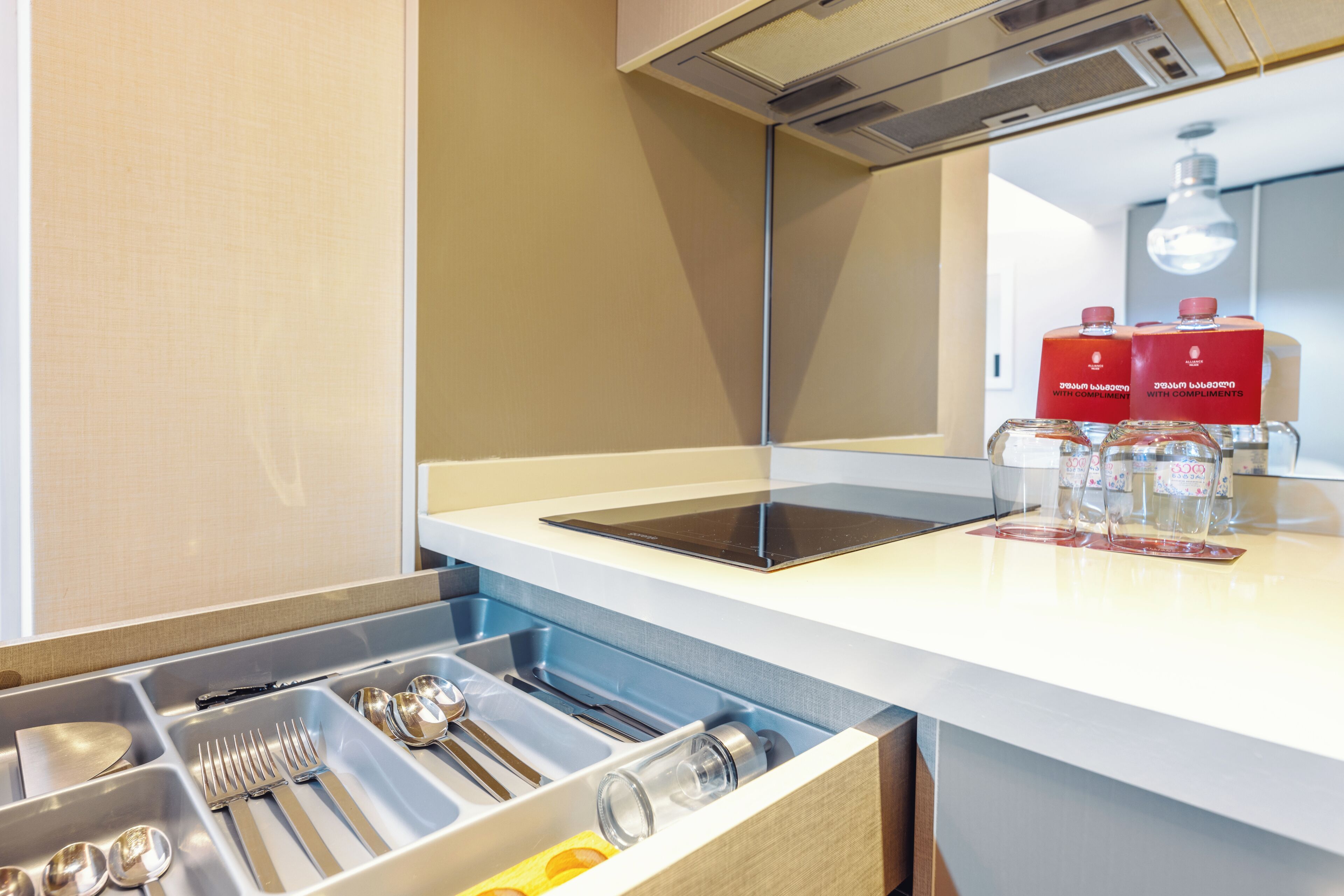 A modern kitchen with a built-in dishwasher, a tablet on the counter, and a drawer with utensils.