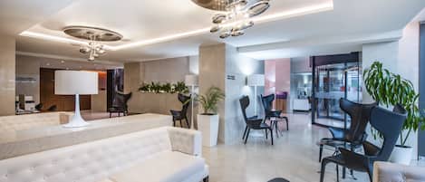 A modern lobby with a white sofa, black chairs, a large potted plant, and a glass table.