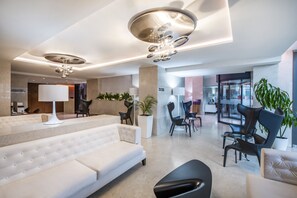 Un vestíbulo moderno con un sofá blanco, sillas negras, una planta grande en maceta y una mesa de cristal.