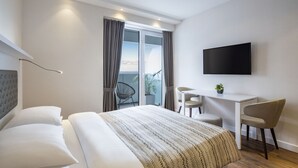 A modern hotel room with a large bed, a desk, a chair, a TV, and a balcony with curtains. - Alliance Palace Batumi (Batumi)