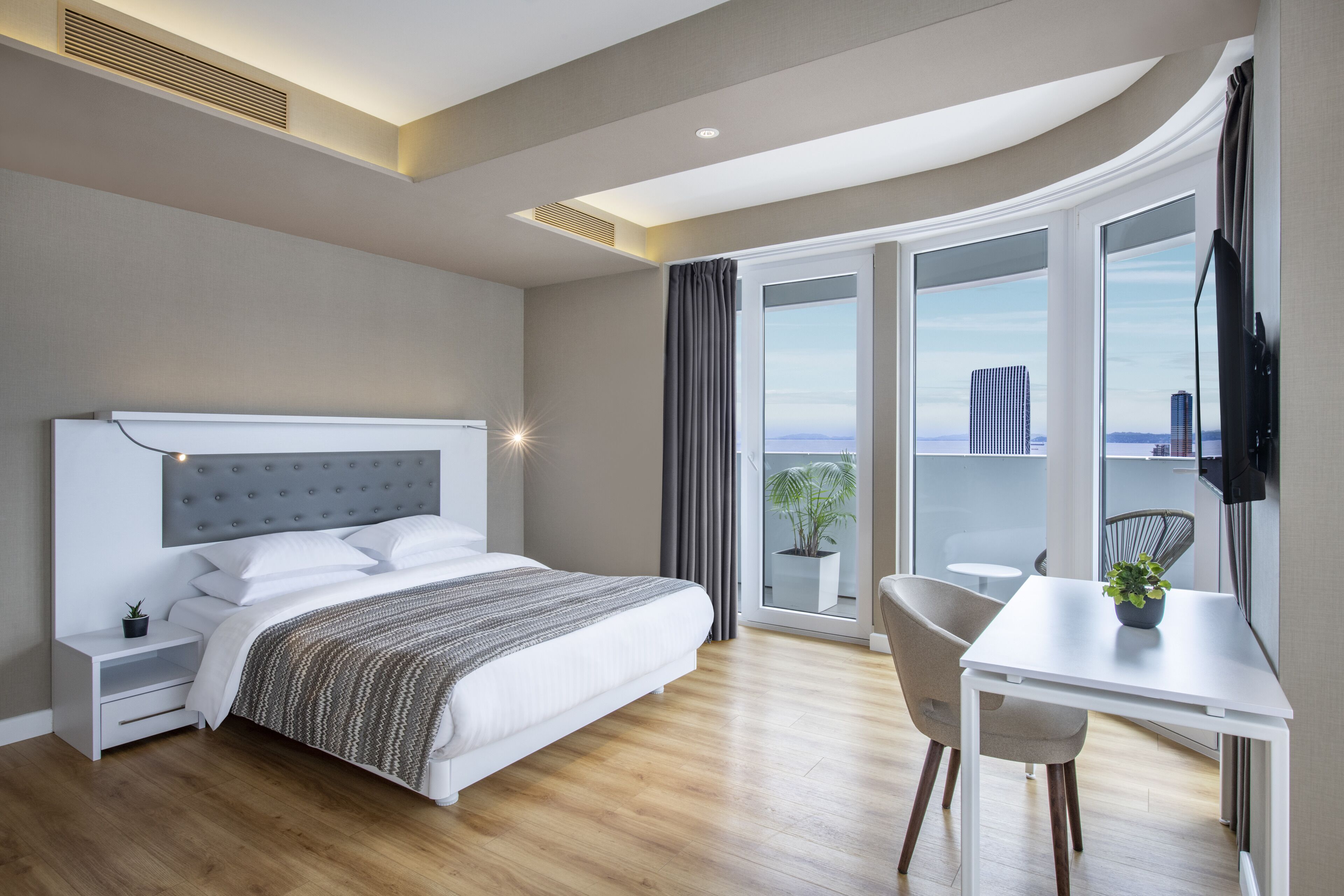 A modern hotel room with a large bed, a desk, and a view of the city.