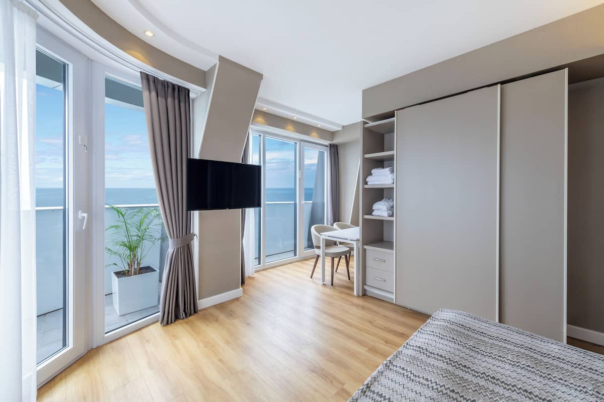 A modern bedroom with a large sliding glass door to a balcony, a bed, a desk, and a wardrobe.