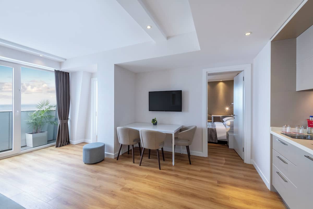 A modern apartment with a dining area, a TV mounted on the wall, and a balcony with a plant.