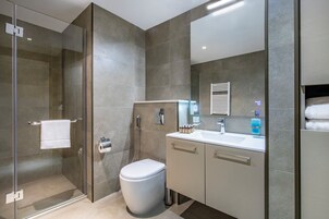 Une salle de bain moderne avec une douche à parois de verre, des toilettes, un lavabo avec un miroir et un porte-serviettes.