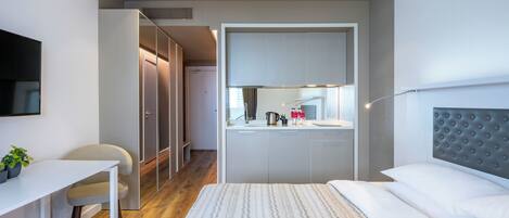 A modern hotel room with a bed, a desk, a chair, and a kitchenette.