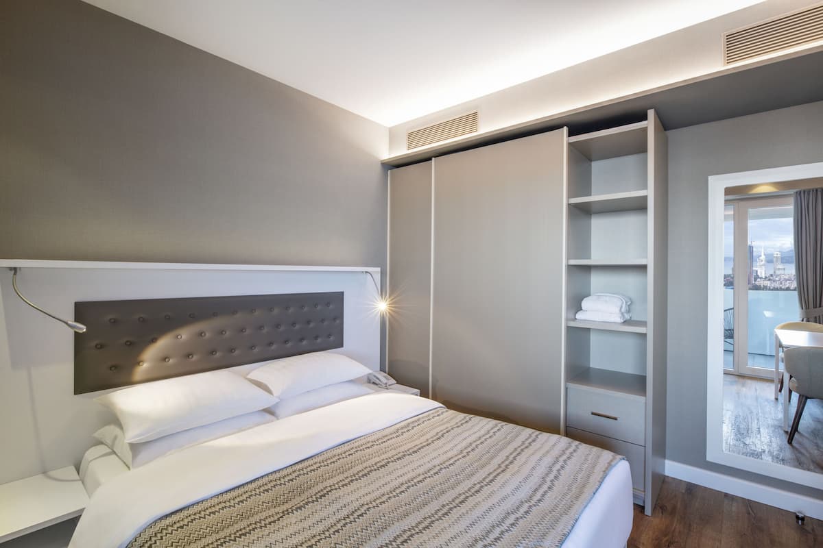 A modern hotel room with a large bed, a built-in wardrobe, and a view of the city through a large window.