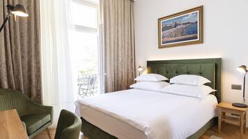 Una habitación de hotel ordenada con una cama grande, un sillón tapizado en verde, una mesita y un escritorio.