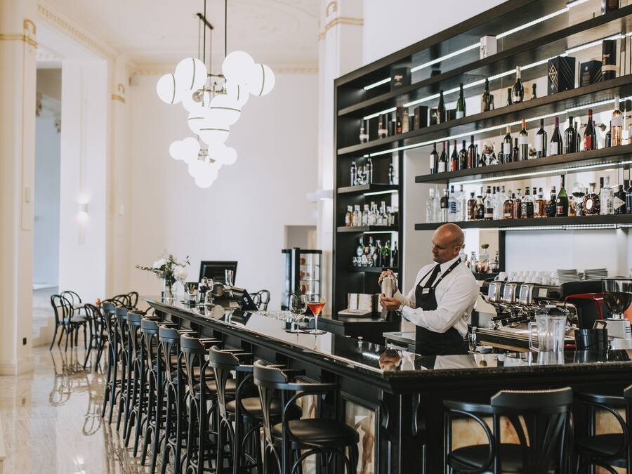 A bar area with a bartender, a long counter, and multiple stools.