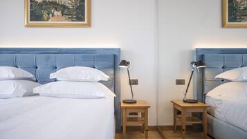 A hotel room with two beds, each with a blue headboard, white linens, and a small wooden nightstand with a lamp.