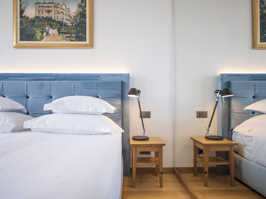 A hotel room with two beds, each with a blue headboard, white linens, and a small wooden nightstand with a lamp.