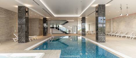 An indoor swimming pool with clear water, surrounded by lounge chairs and a modern interior design.
