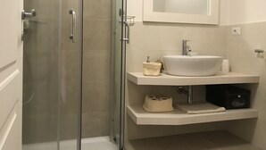 Een moderne badkamer met een douchecabine van glas, een wit wastafelmeubel en een spiegel erboven.
