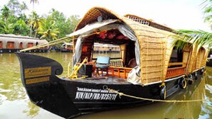A traditional houseboat with a thatched roof, a small deck area, and a visible interior with a table and chairs. - Houseboat Cruise in the Backwaters of Kerala (Kottayam)
