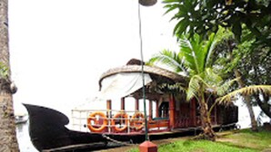 A boat with a thatched roof and orange life rings, docked near a palm tree. - Houseboat Cruise in the Backwaters of Kerala (Kottayam)