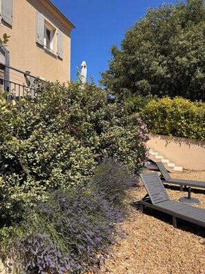 A building with a beige facade, a statue, and a garden with shrubs and a gravel path.