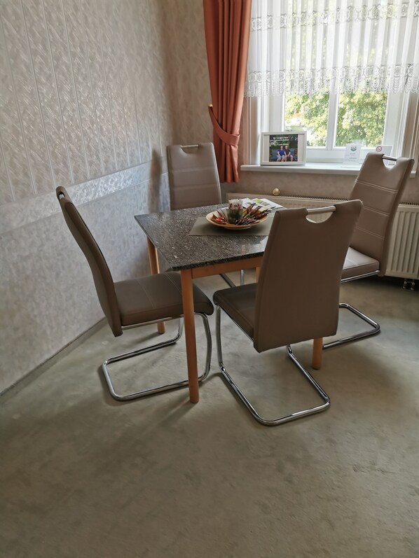 Un coin repas comprenant une table et quatre chaises, une fenêtre avec des rideaux et un radiateur.