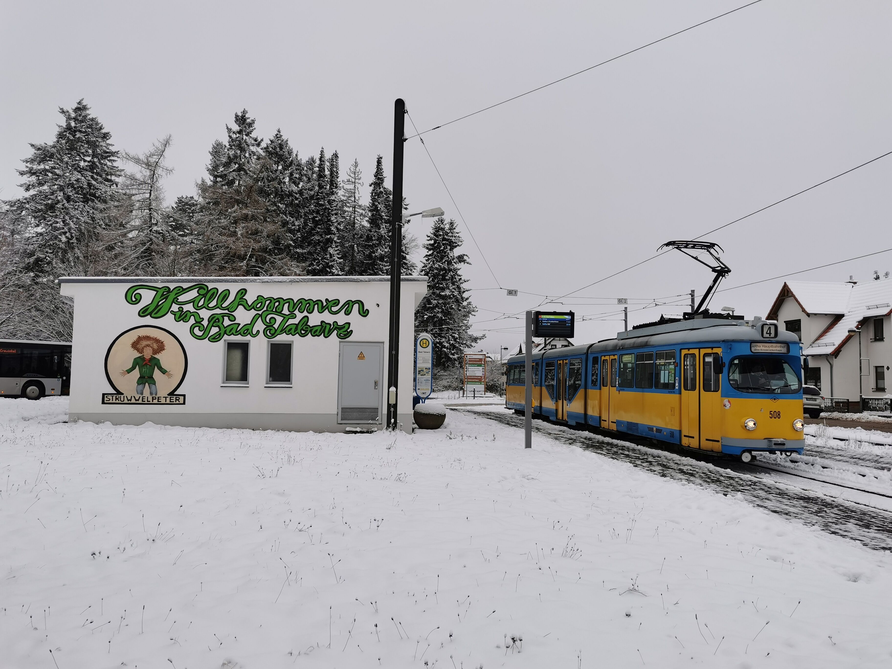 Lumipeitteinen ulkoalue, jossa on raitiovaunu ja rakennus, jonka kyltissä lukee: ”Tervetuloa Bad Tatzbergiin”.