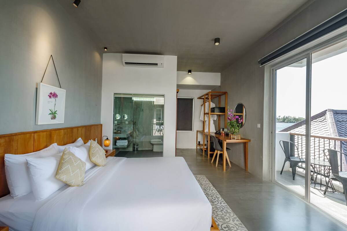 Una habitación de hotel moderna con una cama grande, un escritorio con una silla y un balcón con vistas.
