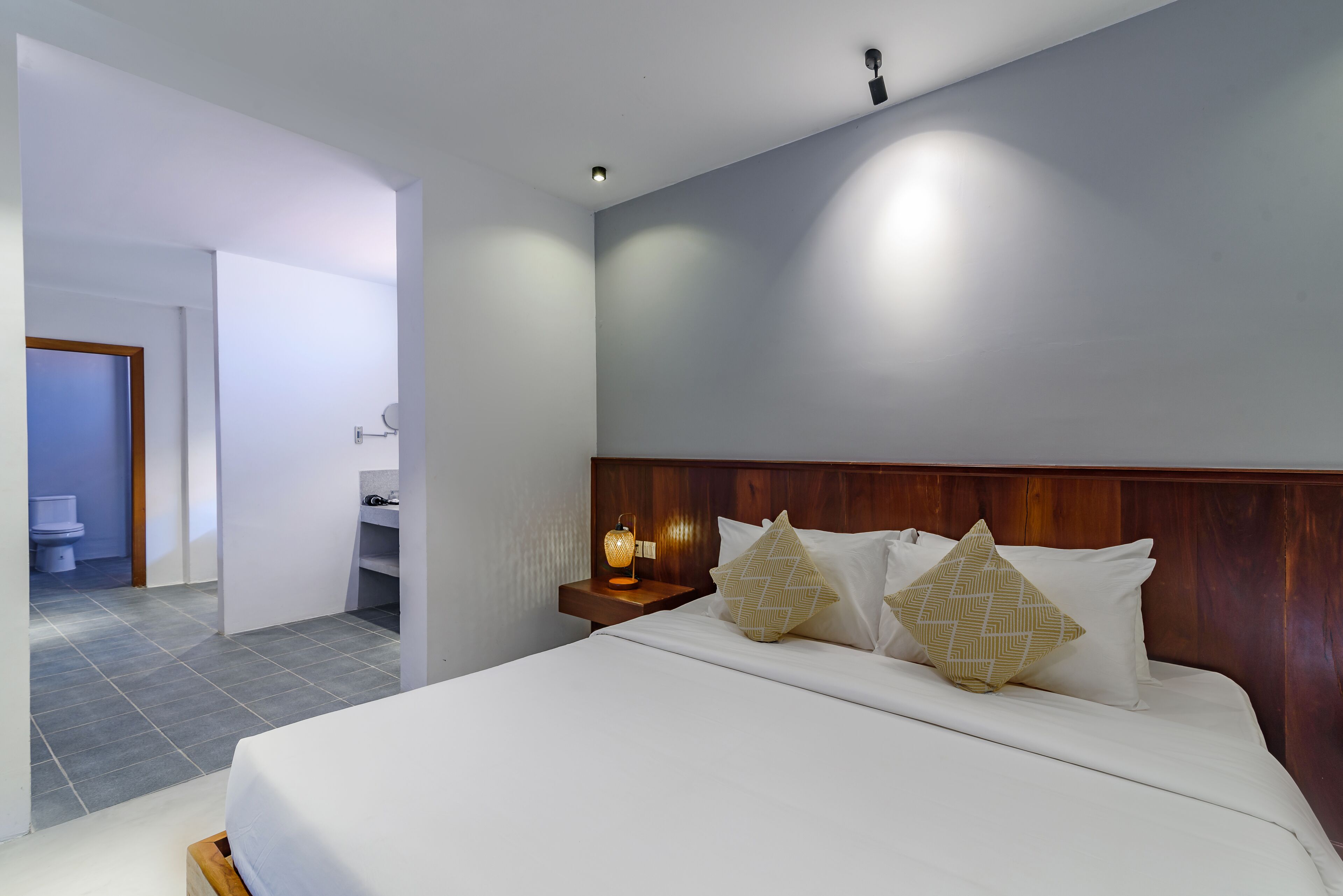 Une chambre d’hôtel moderne avec un grand lit, une tête de lit en bois et une table de chevet avec une lampe.
